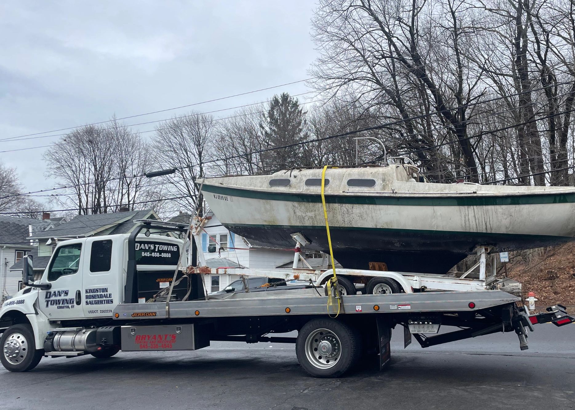 Danny's Towing hauling a trailer and boat on flatbed in Kingston, NY. Secure towing services.