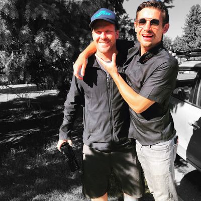 Two men smiling outdoors, one playfully holding the other's face.