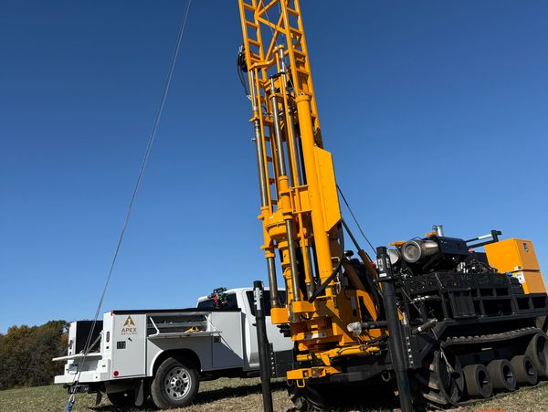 A tall yellow drilling rig and a white service truck on a clear day.