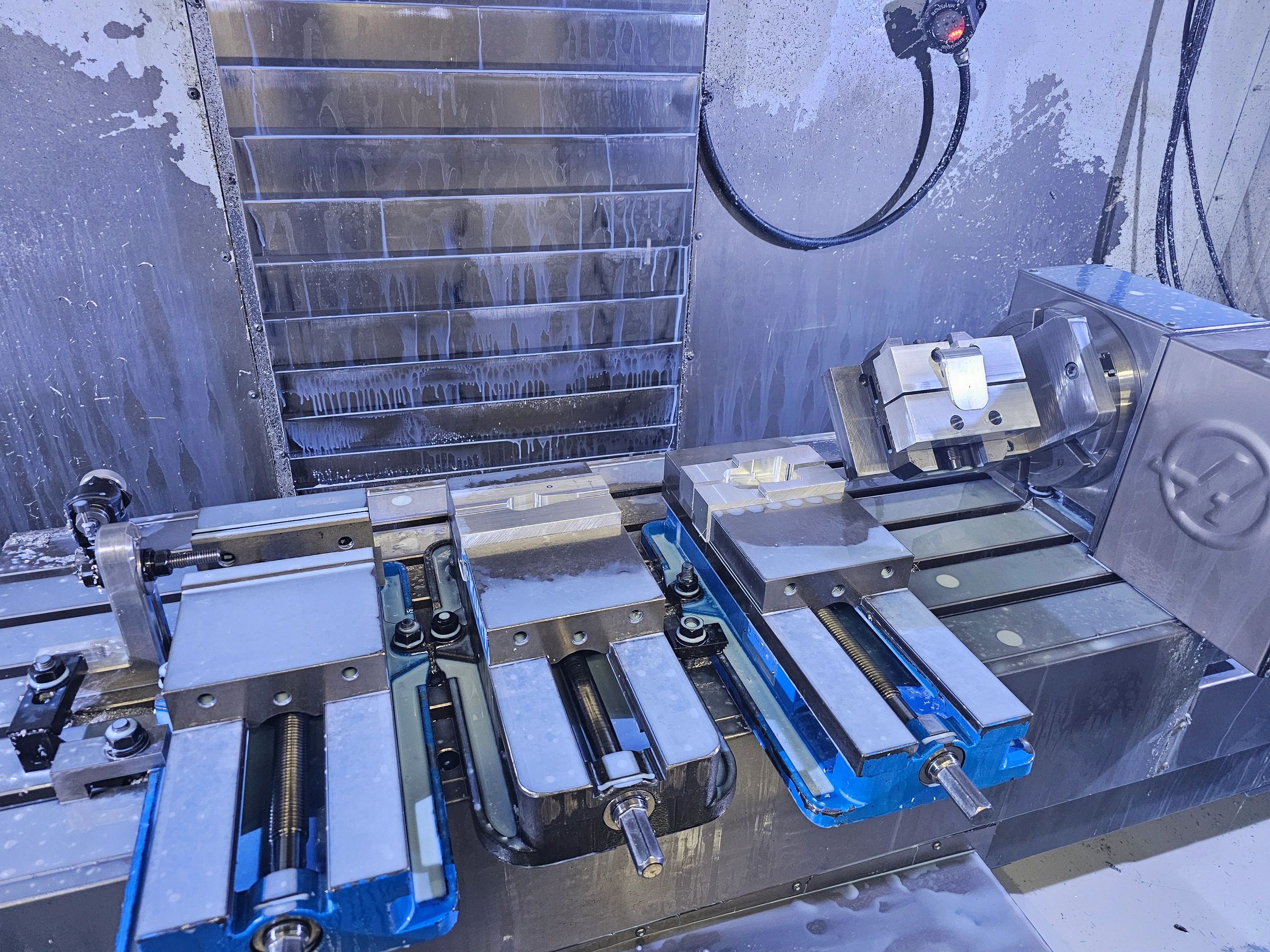 Industrial CNC machine setup with multiple vices and metal fixtures.