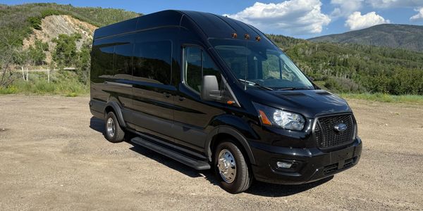 A black Ford van parked on a dirt road with hills in the background.