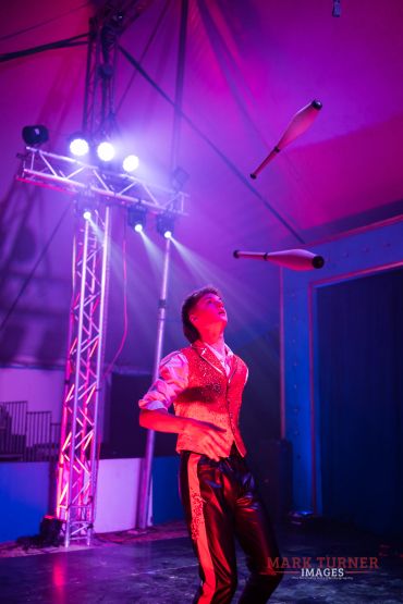 Man juggling clubs under stage lights.
