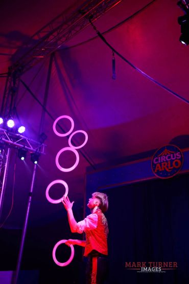 Circus performer juggling rings under colorful lights.