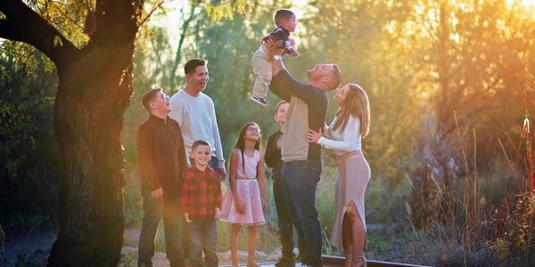 A joyful family moment outdoors during golden hour with a father lifting a toddler.