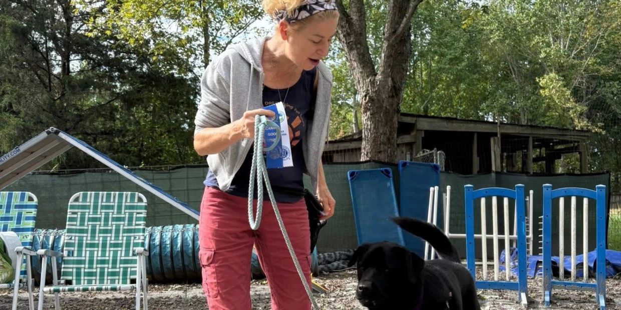 Woman training a black dog outdoors.