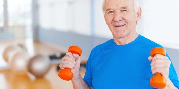 Elderly man exercising with orange dumbbells in a fitness room.