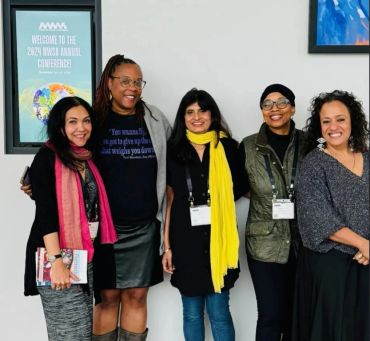 Group of five diverse women smiling indoors.