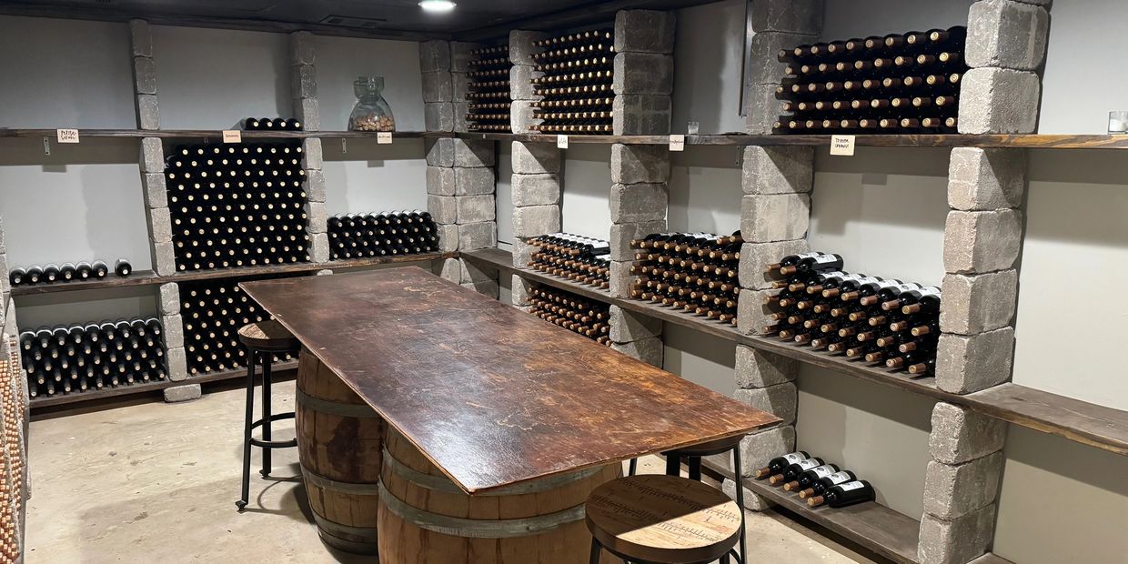 A rustic wine cellar with shelves full of wine bottles and a wooden table on barrels.