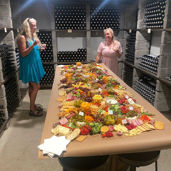 Two women enjoy a large charcuterie spread in a wine cellar.