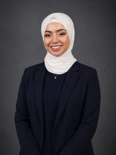 Professional woman wearing a white hijab and dark blazer smiling.