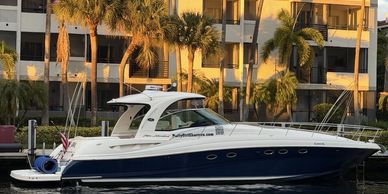 A sleek white and blue yacht docked by a waterfront with palm trees and buildings in the background.