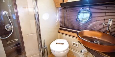 Modern yacht bathroom with glass sink and porthole window.