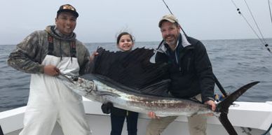 Three people proudly holding a large sailfish on a boat.