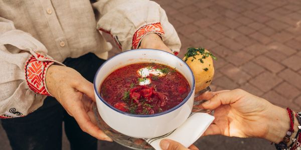 Two people sharing a bowl of beet soup with bread outdoors.