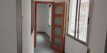 Pasillo con puerta de madera y ventanas con rejas.