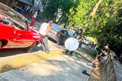 People filming a scene on a sidewalk near cars.