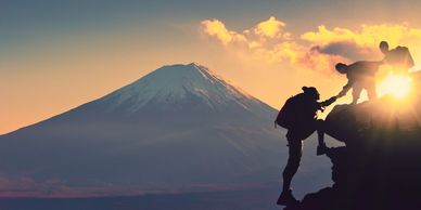 Group of hikers helping someone climb up a rock, with large mountain in the background