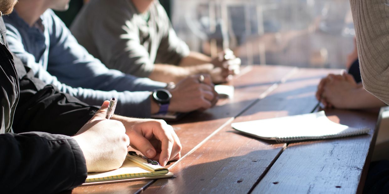 People sitting at a table, writing on notepads