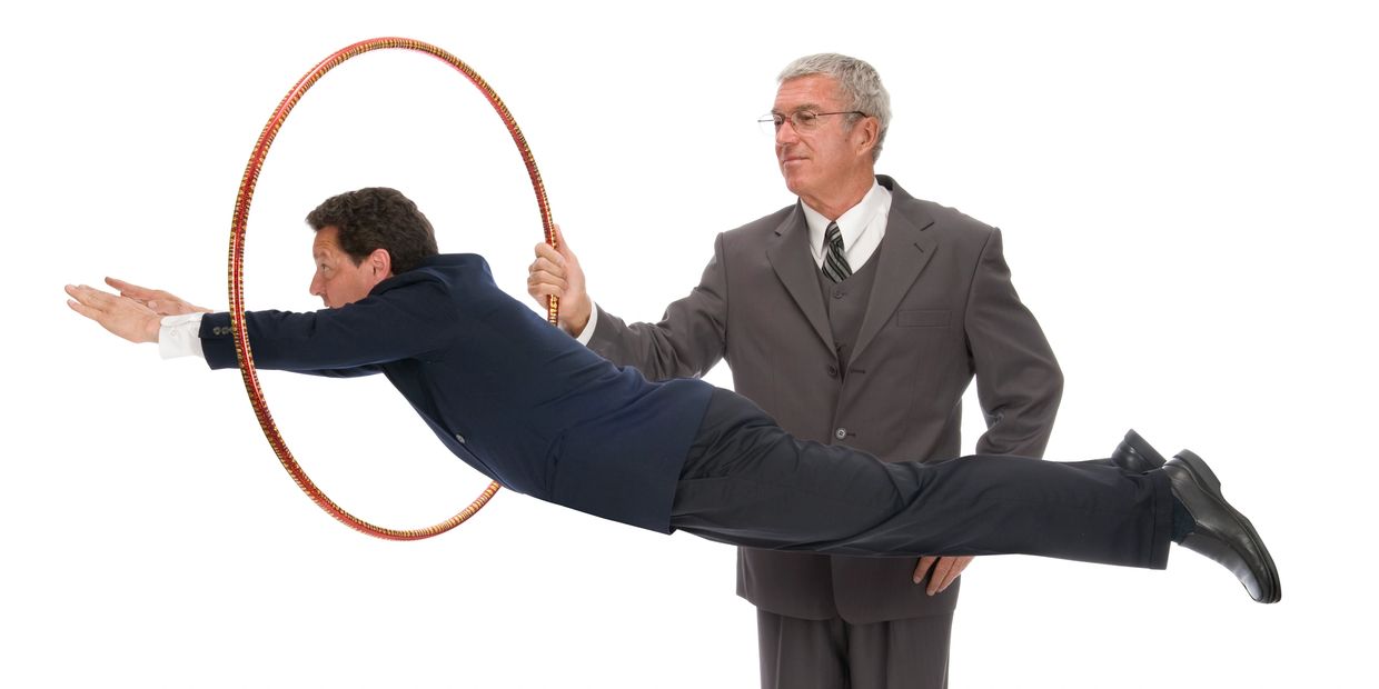 A businessman jumps through a hoop held by another businessman