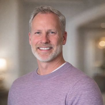 Smiling middle-aged man in a lavender sweater indoors.