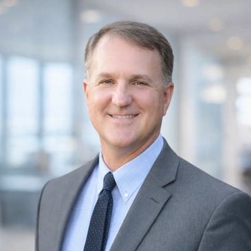 Professional man in a gray suit smiling confidently indoors.
