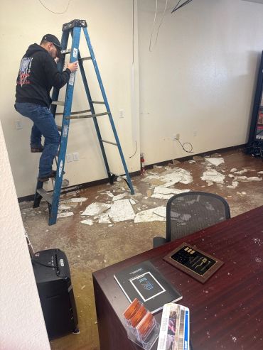 Man climbing a ladder in a room with ceiling tiles on the floor.