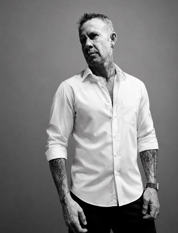 Tattooed man in a white shirt posing.