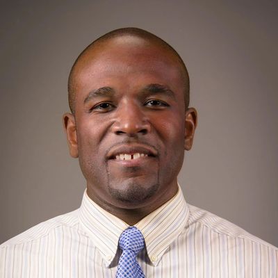 Confident man in a striped shirt and blue tie smiles at the camera.