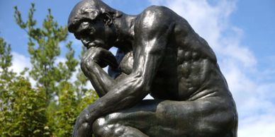 The Thinker statue by Auguste Rodin against a blue sky.