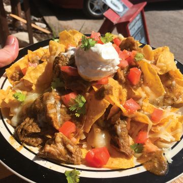 Plate of loaded nachos with cheese, chicken, tomatoes, cilantro, and sour cream.