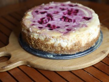 A berry-topped cheesecake on a wooden board.