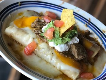 Plate of enchiladas topped with ground beef, cheese, guacamole, sour cream, and tomato.