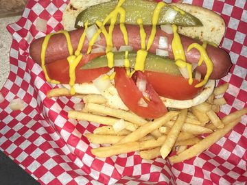 Hot dog topped with mustard, pickles, onions, and tomato with a side of fries.