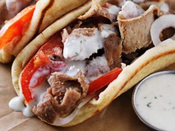 Close-up of gyro sandwiches with meat, tomato, onion, and white sauce.