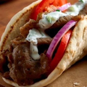 Close-up of a gyro sandwich with meat, tomato, onion, and tzatziki sauce.