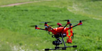 Drone with 2 cameras flying over green field.