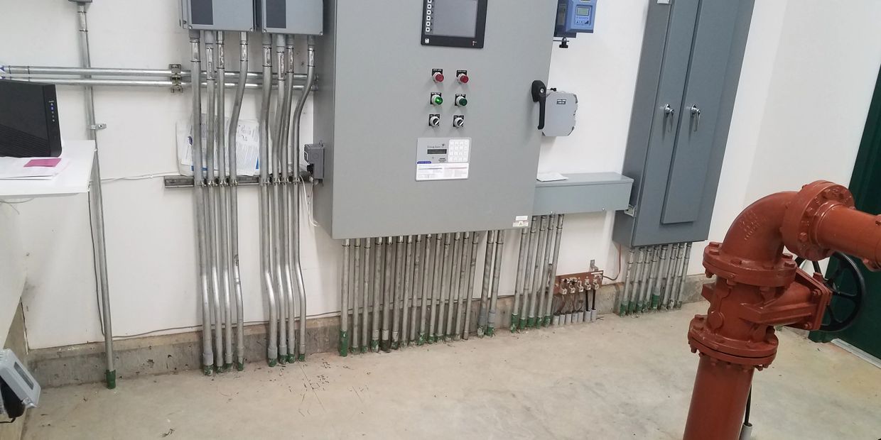 Industrial control panel with metal conduit pipes and a red valve in a utility room.