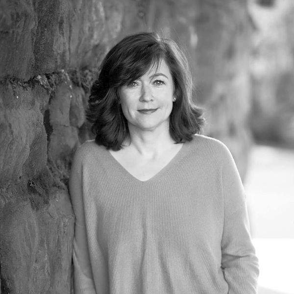 Woman in a sweater leaning against a stone wall, black and white portrait.