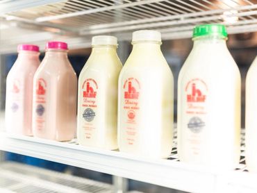 Rows of milk bottles in a refrigerator with pink and green caps.