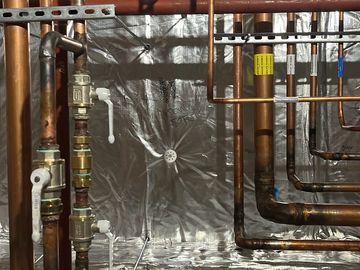 Copper pipes with labels indicating medical suction and compressed air in an industrial setting.