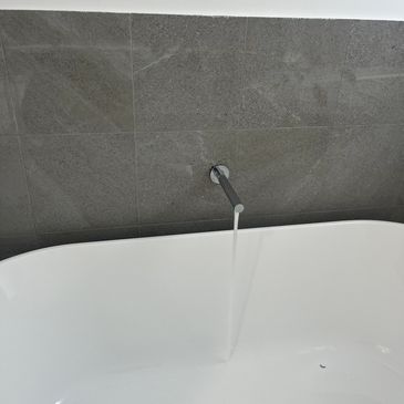 Minimalist bathroom with a white bathtub and water flowing from a wall-mounted faucet.