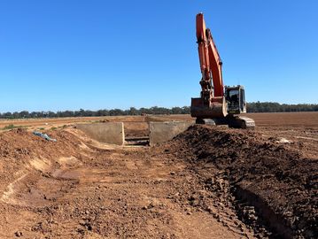 Excavator working on a large dirt field under a clear blue sky.
