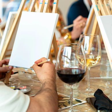 People painting on canvases while enjoying glasses of wine.