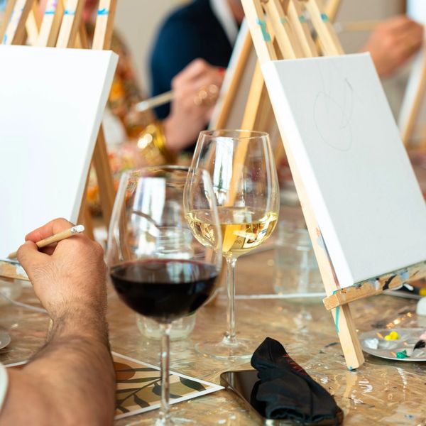 People painting on canvases while enjoying glasses of wine.