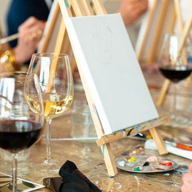 People painting on canvases while enjoying glasses of wine.