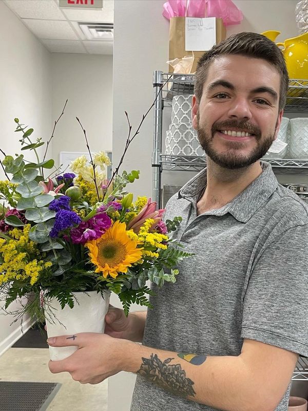Smiling man holding a vibrant flower arrangement in a shop.