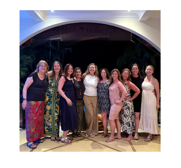 A group of ten women posing together under an archway at night.