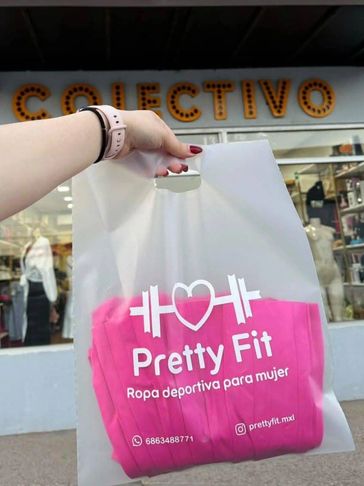 A hand holds a Pretty Fit plastic bag with pink sportswear inside outside a store.