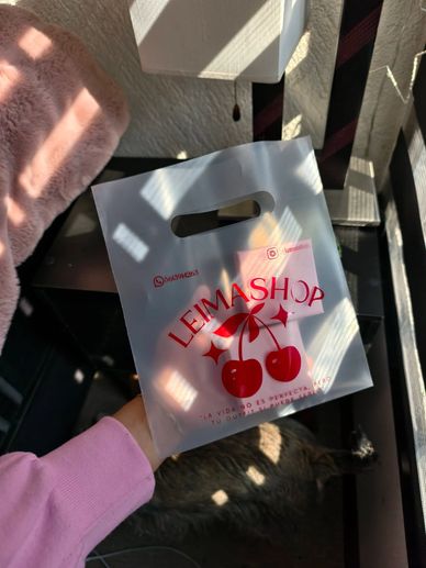 Hand holding a translucent shopping bag with cherries and LEIMASHOP logo.