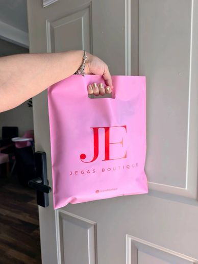 Hand holding a pink shopping bag from Jegas Boutique.